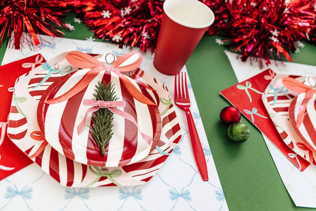 Festive Christmas table setup featuring red and white ornament-shaped plates, red cups, and green placemats from the Festive Fun Co. Ornaments & Bows Collection — perfect for a modern holiday party look.
