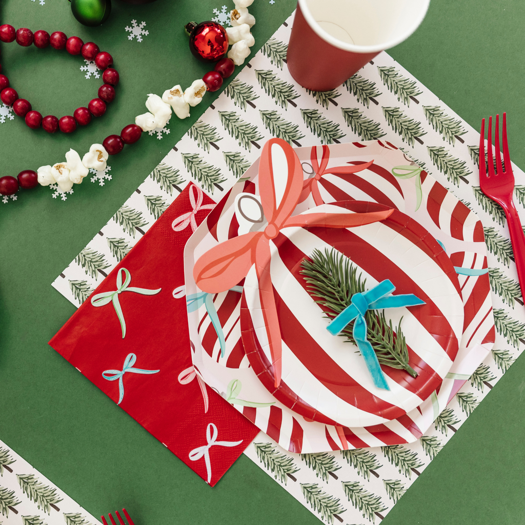 Christmas-themed table setting with red and white striped plates, napkins, and greenery on a green tablecloth.
