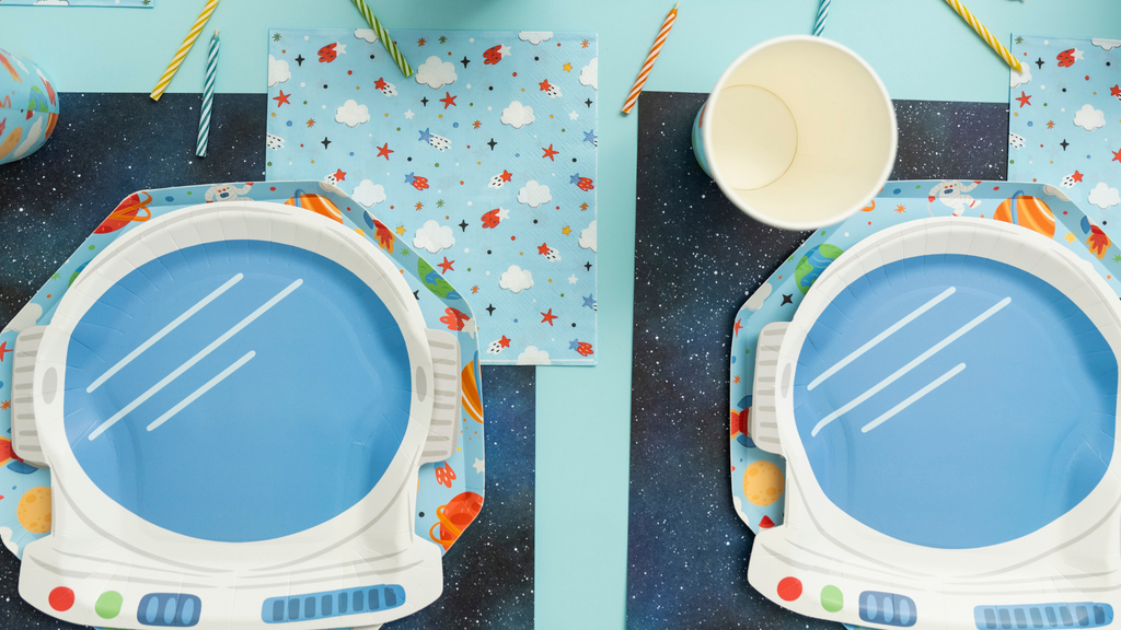 Space-themed tableware set with blue plates, white bowls, and colorful placemats on a blue background.